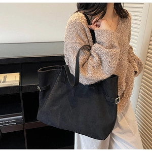 Close-up of black suede tote bag with side buckles held by a model in casual attire