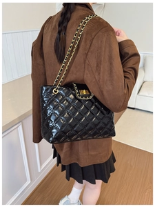 Quilted black leather tote bag with gold chain strap shown on model's shoulder