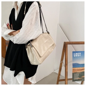 Detail of cream chain flap bag with textured stitching and dark metal strap on model