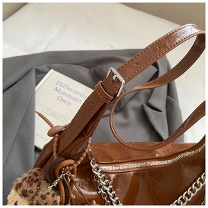 Dettaglio borsa sottobraccio in vernice marrone con catena argento e ciondolo leopardato