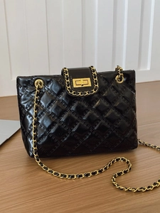 Black quilted tote bag with gold chain straps and metal twist lock on a wooden table