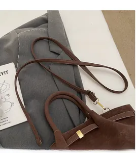 Détail d'un sac à main vintage en cuir marron avec bandoulière sur blazer gris