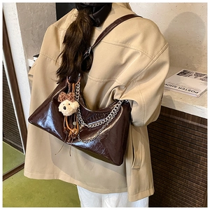 Modella indossa borsa hobo in vernice marrone scuro con catena argento e orsetto peluche