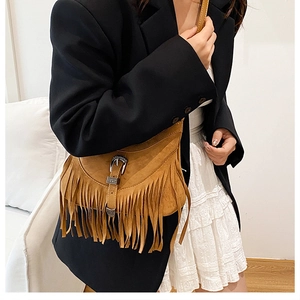 Close-up of brown suede crossbody bag featuring vintage metal buckle and long tassels