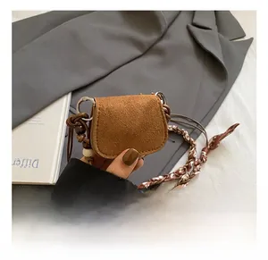 Detail of a brown suede mini saddle bag with woven bead strap and silk scarf accents