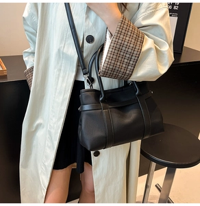 Detail of black pebbled leather tote bag with decorative strap and adjustable shoulder strap