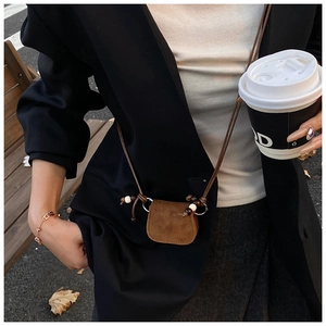 Detail of a brown suede mini crossbody bag with a slim strap and decorative wooden beads