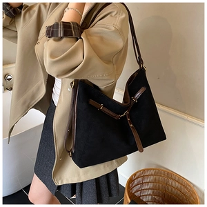 Detail of minimalist black suede tote bag with brown leather straps and gold buckle