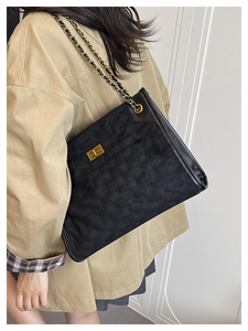 Detail of black quilted suede tote bag with gold chain strap and metallic twist lock