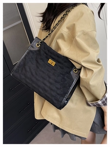 Detail of black quilted tote bag with gold chain strap and turn-lock on shoulder