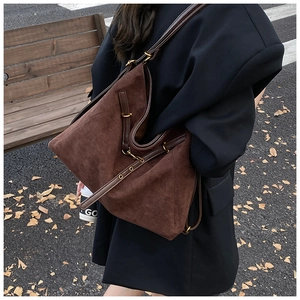 Street style view of a large dark brown suede tote bag with golden metal buckles