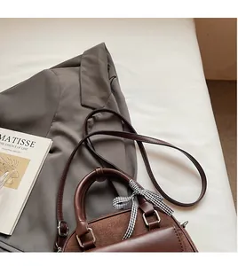Détail du sac bowling en cuir marron foncé avec ruban à nœud et bandoulière réglable