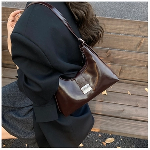 Detail van donkerbruine glanzende crossbodytas met zilveren gesp gedragen door model