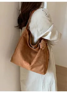 Detalle de un bolso tote de ante marrón con un colgante de oso de peluche y etiqueta de cuero