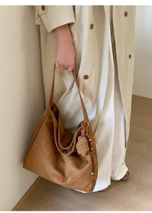 Detalle de bolso tote de ante marrón con colgante de oso y correa de cuero en modelo
