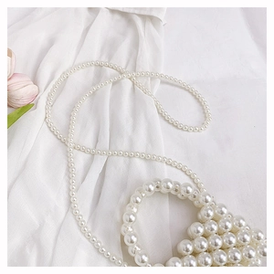 Detail of hand-woven faux pearl handbag with round top handle and elegant long shoulder strap