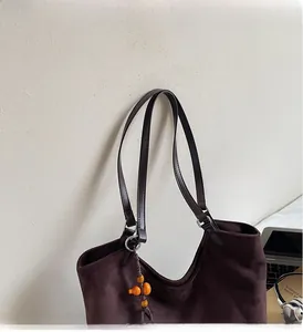 Détail du sac cabas en suède avec poignées en cuir foncé et breloque citrouille