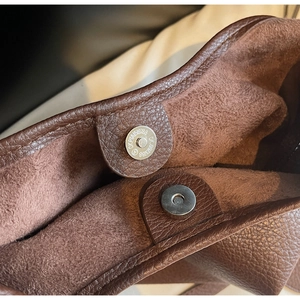 Macro detail of silver magnetic snap closure on a brown pebble leather hobo bucket bag