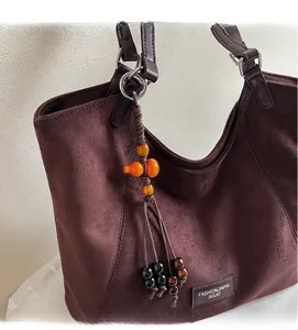 Gros plan d'un sac cabas en daim marron foncé avec breloques artisanales et logo cuir