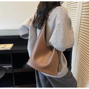 Brown lychee grain leather hobo bag with round charm shown on model in a casual setting