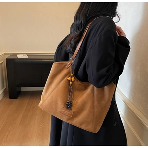 Détail d'un sac cabas en daim marron avec un pendentif décoratif en perles de bois et glands