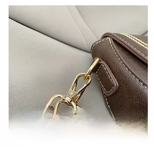 Detail of gold metal buckle and white contrast stitching on brown leather saddle bag