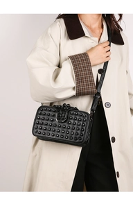 Détail d'un sac bandoulière en cuir noir avec rivets décoratifs et fermoir en U argenté