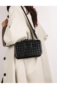 Détail d'un sac bandoulière noir à rivets avec fermoir métallique en forme d'anneau