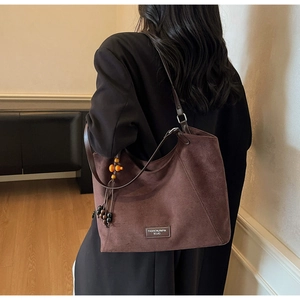 Détail du sac bandoulière en daim avec perles en bois et pompon tissé élégant