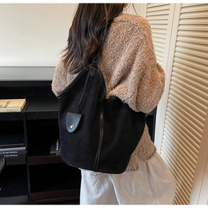 Detail of vintage black suede tote bag with glossy leather trim worn by model