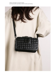 Détail du sac bandoulière noir à rivets porté sur un trench-coat beige élégant