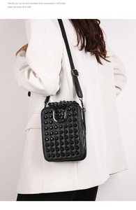 Détail d'un sac bandoulière noir avec rivets et bandoulière réglable sur manteau blanc