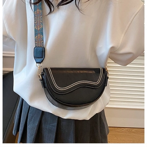 Detail of black saddle bag featuring studded wavy edges and colorful woven guitar strap