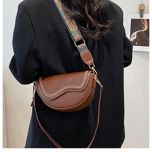 Detail of dark brown saddle bag with patterned wide strap and slim leather strap