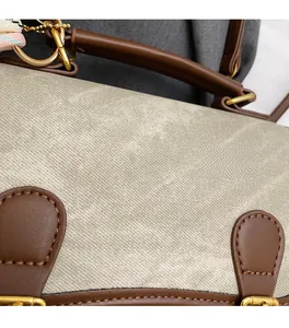 Gros plan du sac bandoulière en tissu beige avec garniture en cuir brun et boucle dorée