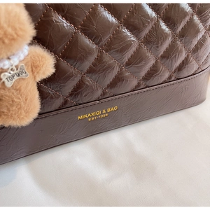 Vue macro d'un cabas matelassé marron foncé avec logo doré et charm d'ours en peluche
