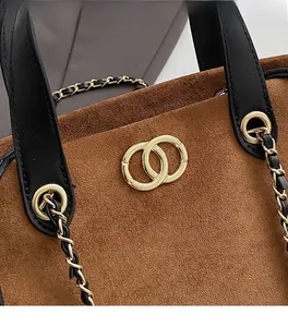 Close-up of brown faux suede tote bag with gold logo hardware and black leather strap