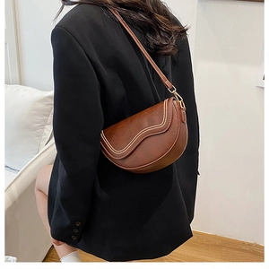 Brown saddle bag with double stitching and gold hardware shown on model in black suit