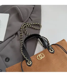 Detailed shot of brown suede tote bag featuring a gold buckle and black chain shoulder strap