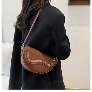 Detail of a brown saddle bag featuring wavy gold rivet studs and a slim shoulder strap