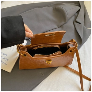 Macro detail of brown pleated leather handbag with golden ring lock on grey blazer