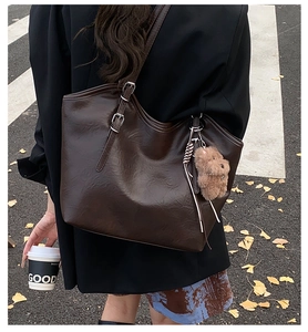 Details einer braunen Vintage-Einkaufstasche mit Bärenanhänger und verstellbarem Gurt