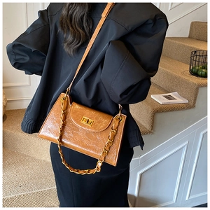 Detail of brown glossy textured shoulder bag with gold twist lock and chain strap