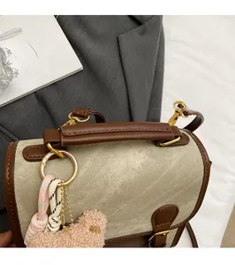Détail du sac à dos en toile avec poignée en cuir brun et breloque ours en peluche