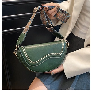 Detail view of dark green leather saddle bag featuring ethnic patterned wide strap and gold hardware