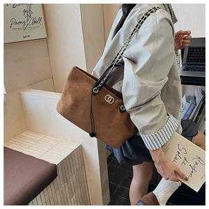Macro detail of brown faux suede tote bag with metal logo and elegant chain strap
