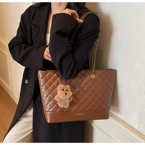 Détail d'un cabas matelassé marron avec lettrage doré et breloque chiot en peluche