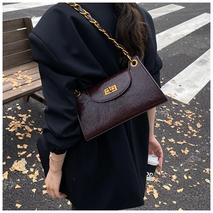 Burgundy crinkled patent leather shoulder bag with gold chain strap on a model