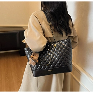 Détail du sac cabas matelassé noir avec chaîne dorée et breloque ours en peluche sur modèle