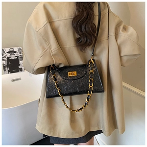 Detail of glossy black quilted bag with gold chain and turn-lock worn by a model